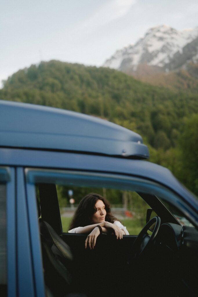 Woman gazing from car window, surrounded by scenic mountains and lush greenery.